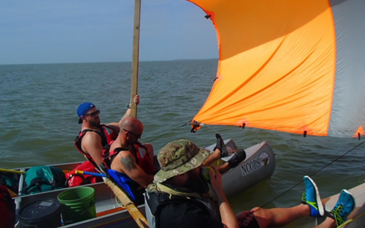 three people sit in canoes using a tarp as a makeshift sail